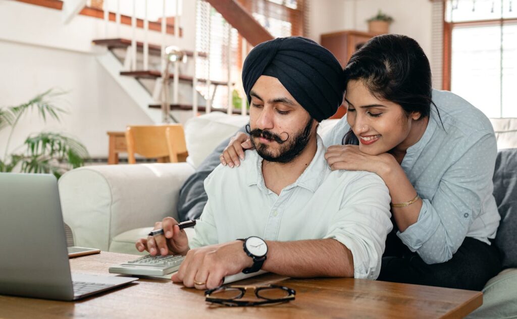 Cheerful ethnic couple using calculator while sitting at table